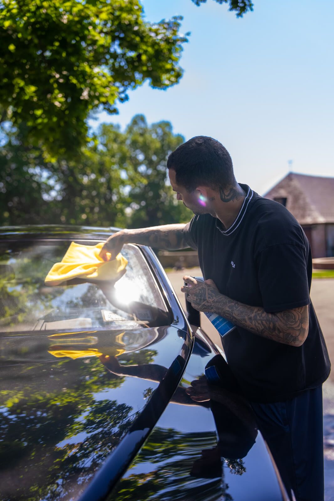Detailer wiping a black Audi windshield with strong sun flare through the glass