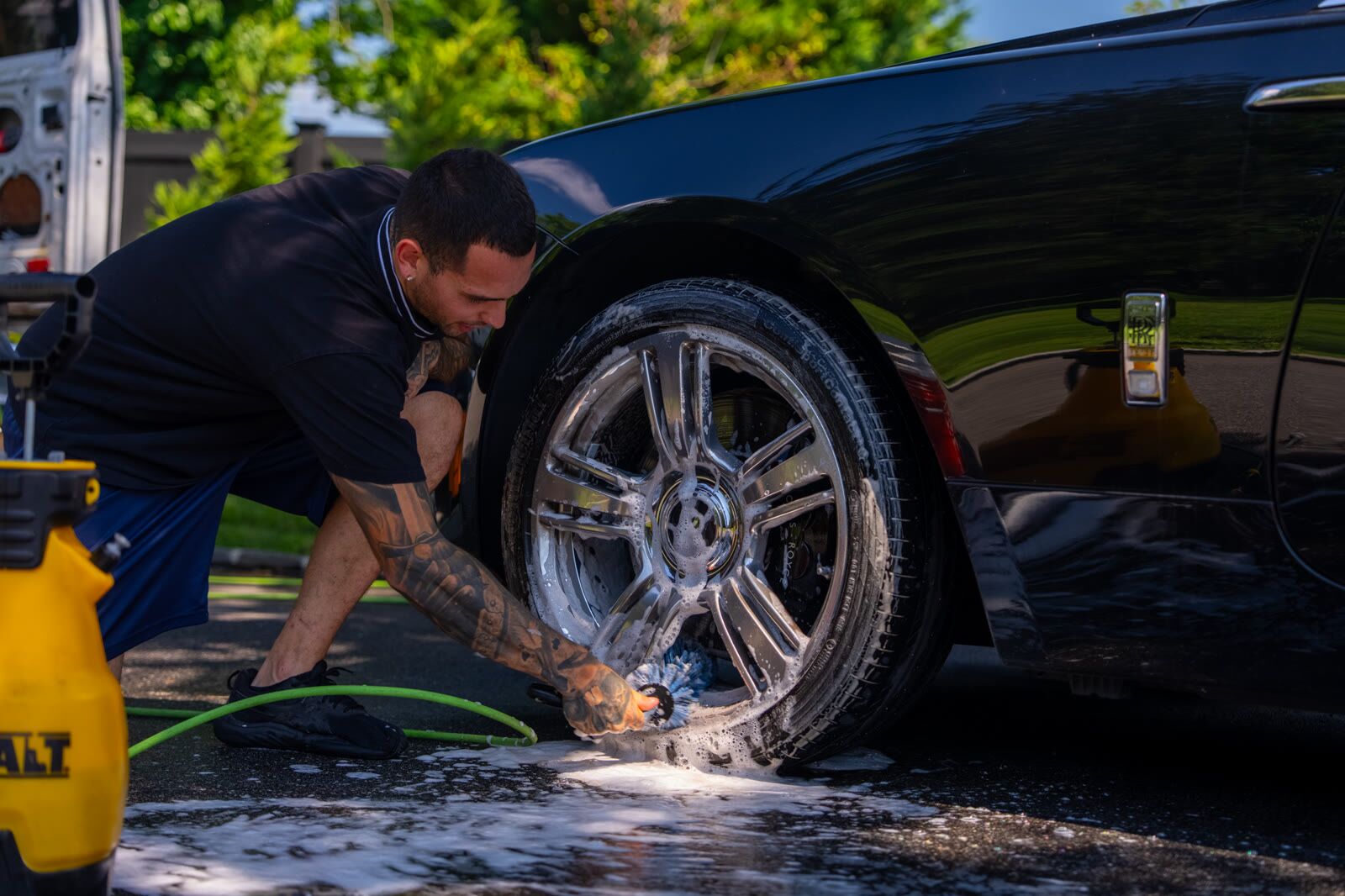 Detailer scrubbing a Rolls-Royce Wraith wheel with foam and a rim brush