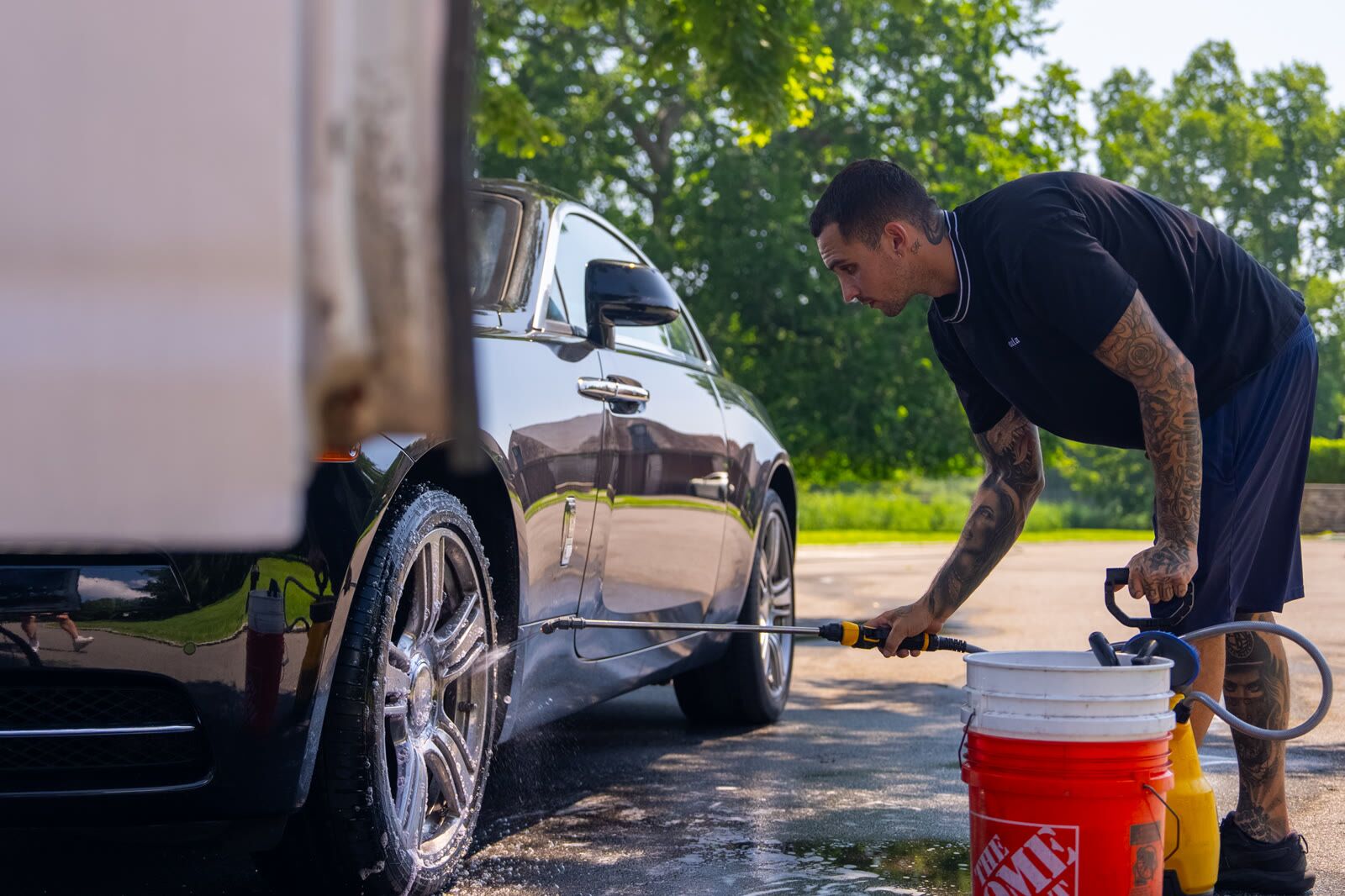 Detailer rinsing a Rolls-Royce Wraith wheel and tire with a garden hose
