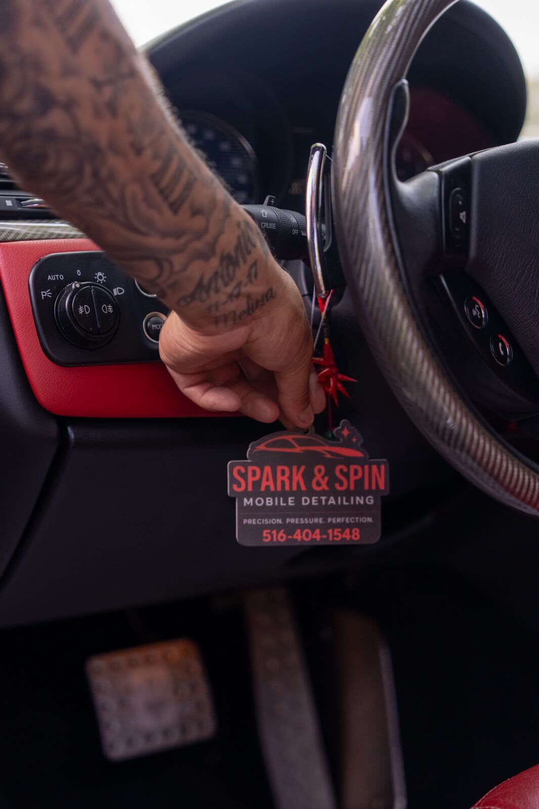 Spark & Spin branded air freshener being hung inside a Dodge cabin with red trim and a carbon-fiber steering wheel